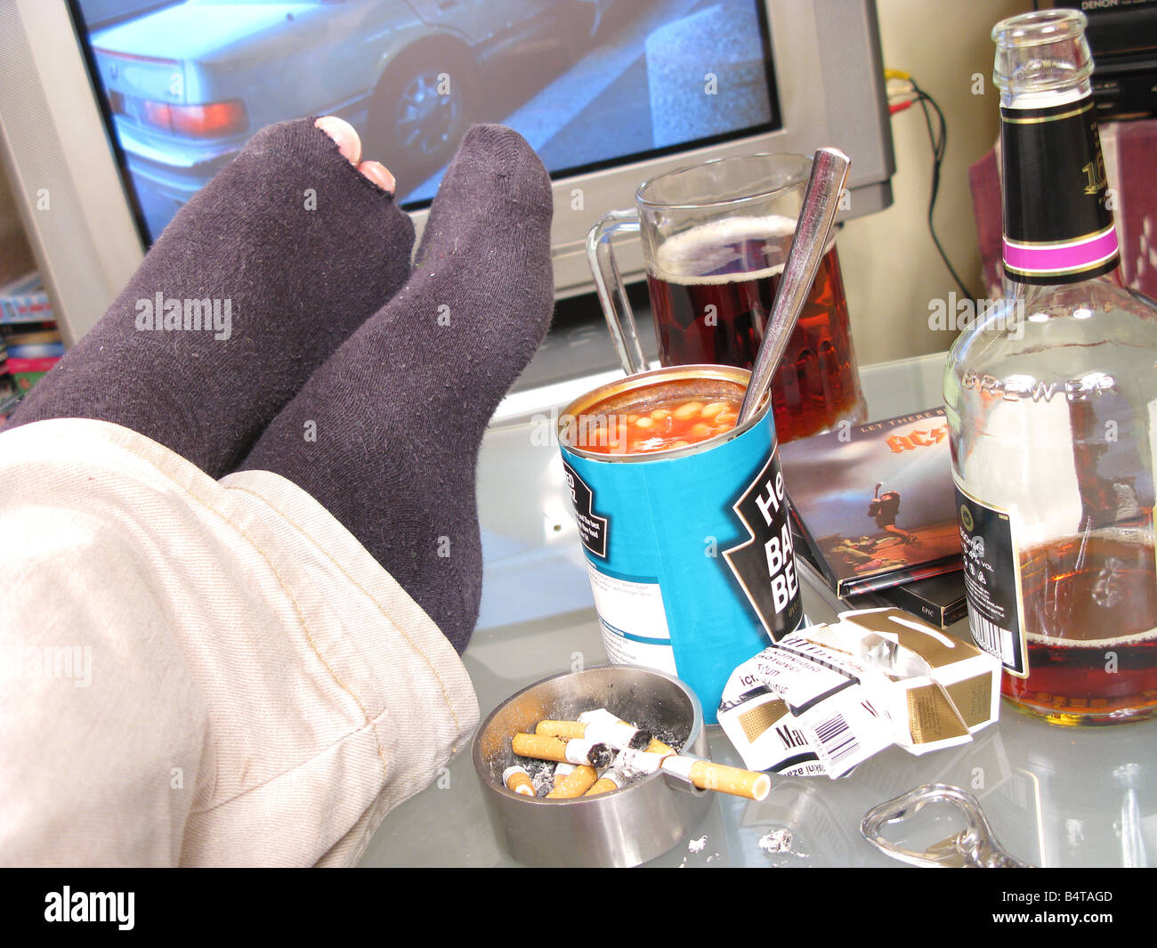 Feet up on an untidy table in a bachelor pad, with toes showing through a torn sock. Stock Photo