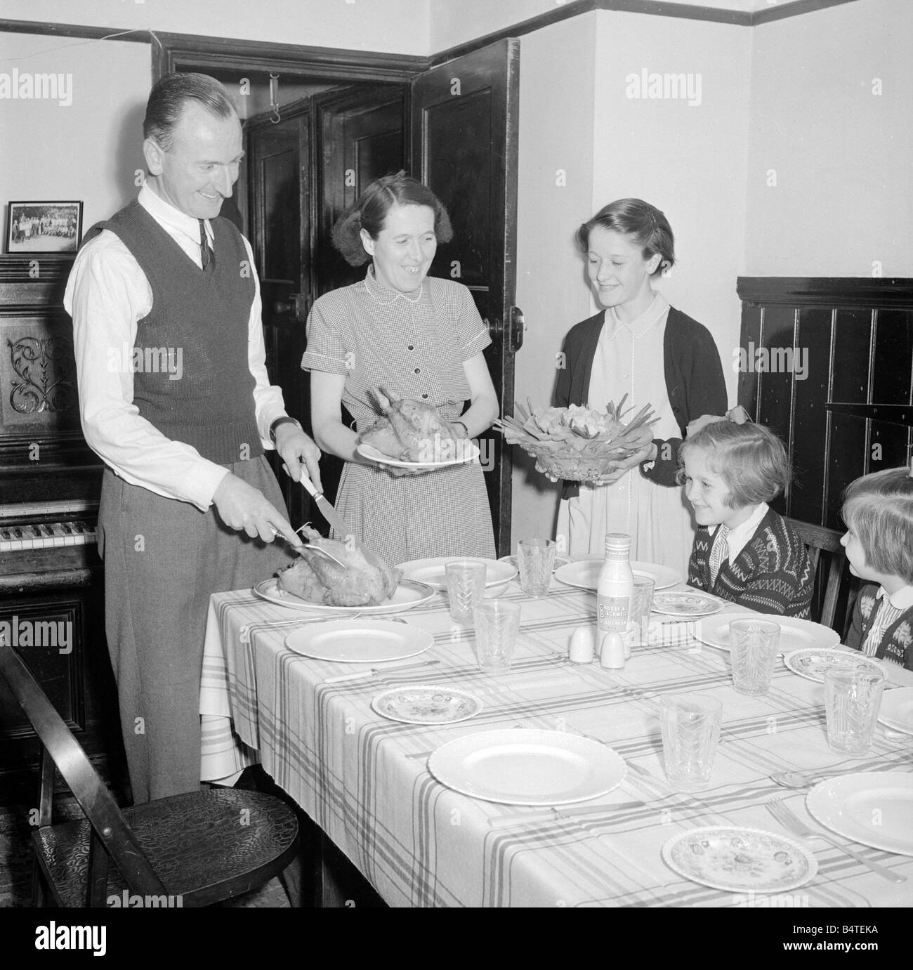 Dad carves the chicken as mum and eldest daughter brings in the vegtables for lunch Circa 1957 Stock Photo
