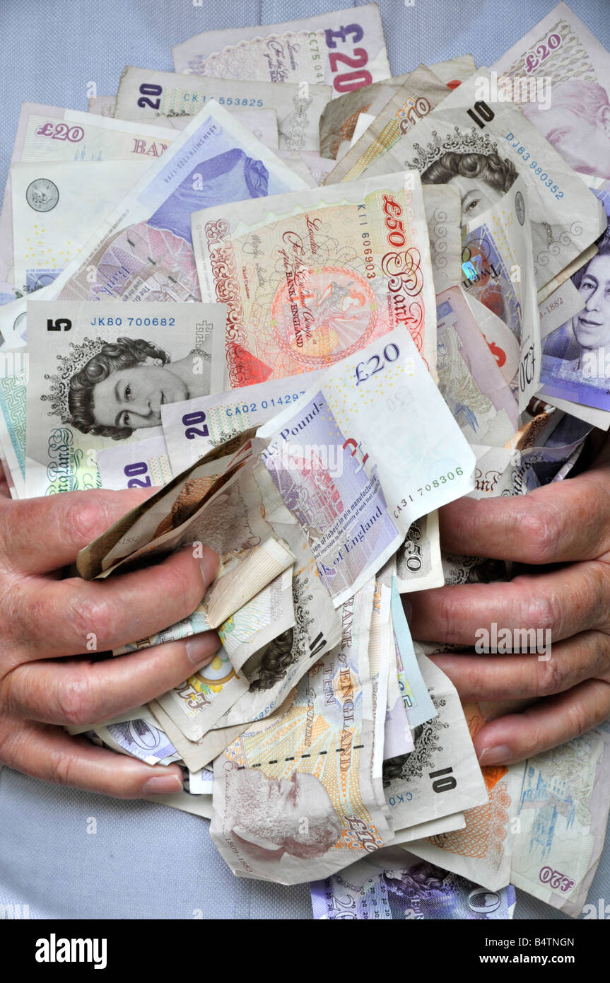 Pile of cash made up of assorted sterling UK pound currency bank notes with hands holding money to mans chest and held by grasping fingers England Stock Photo