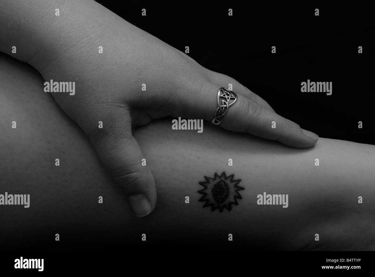 womans hand with pentacle shaped ring on tattooed leg Stock Photo