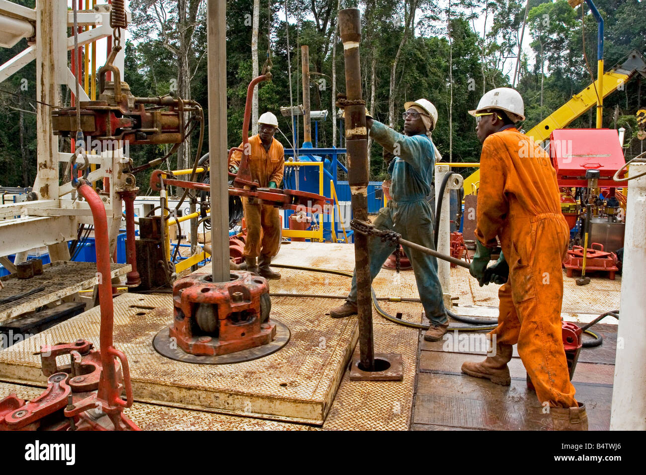 Remote jungle rainforest onshore oil and gas rig site with workers lifting  sub connector for pipe with chain tong, Gabon, Africa Stock Photo - Alamy