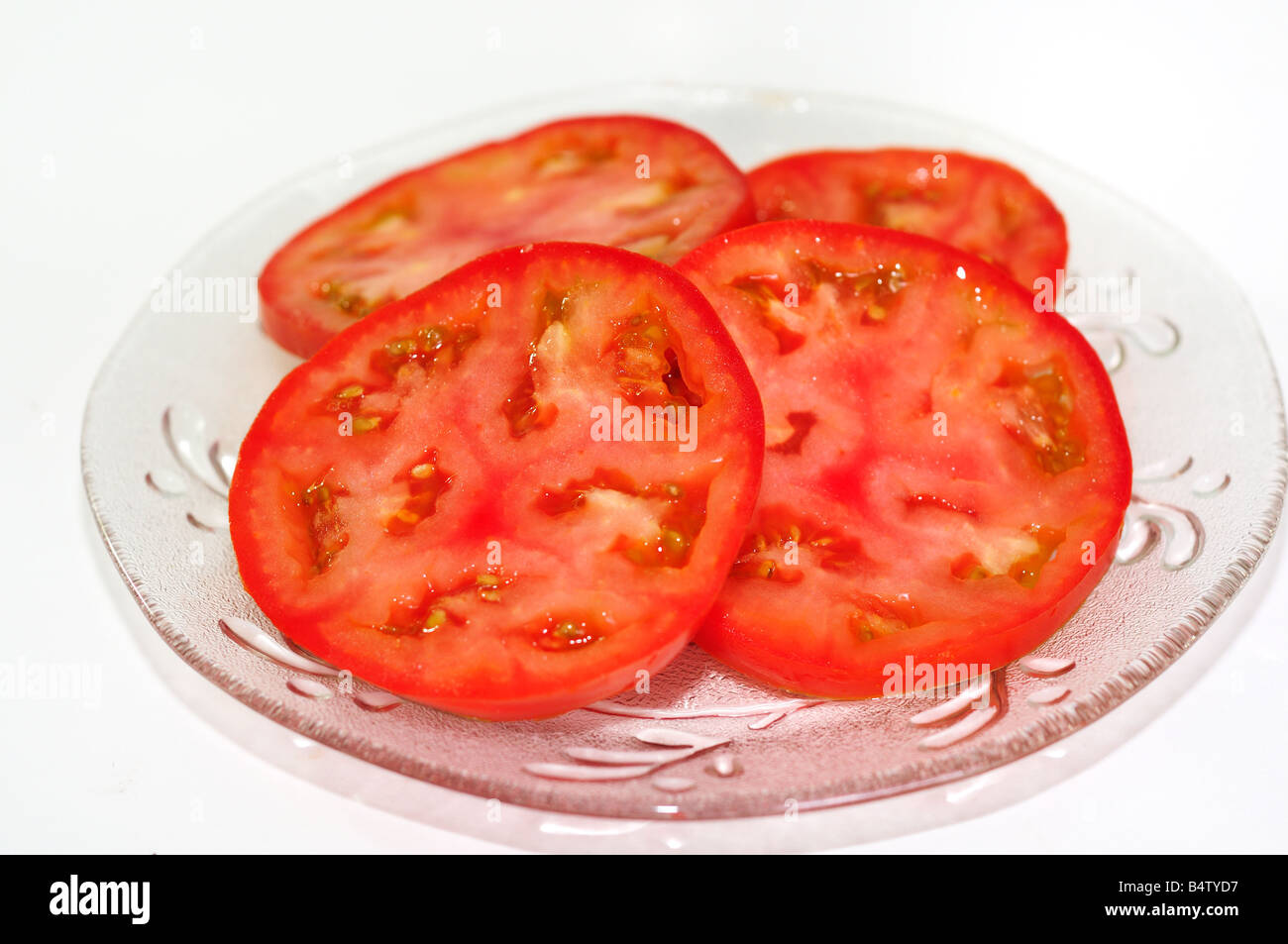 Organic home-grown sliced fresh tomatoes on a clear cut-glass plate. Closeup. Stock Photo
