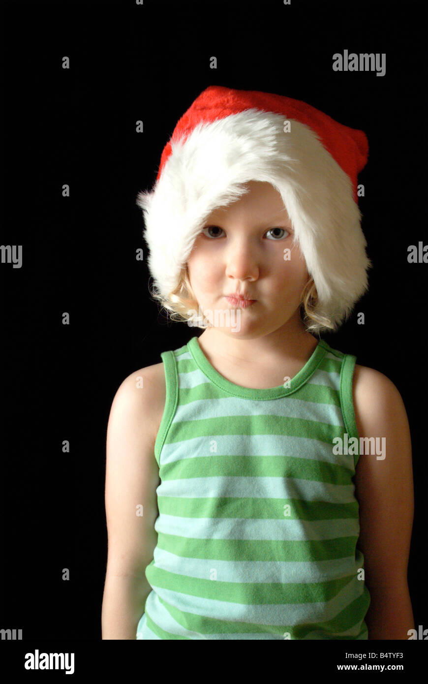 White girl wearing a red christmas hat and green stripy vest, looking apprehensive. Stock Photo