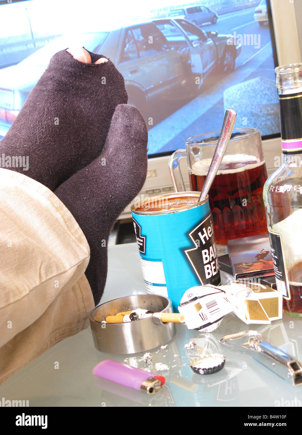 Feet up on an untidy table in a bachelor pad, with toes showing through a torn sock. Stock Photo