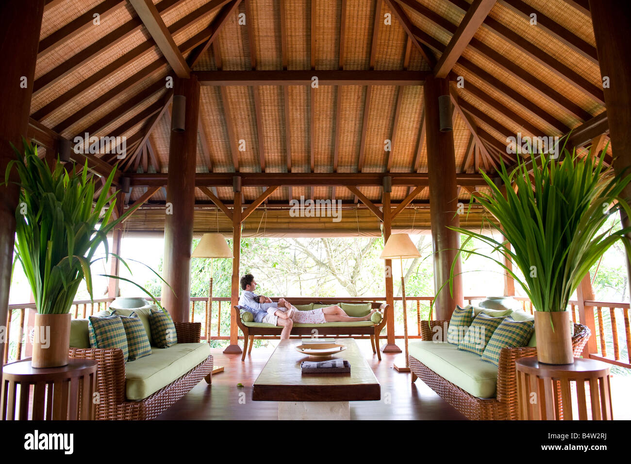 A couple lounges in an open air living room set in a tropical forest. Stock Photo