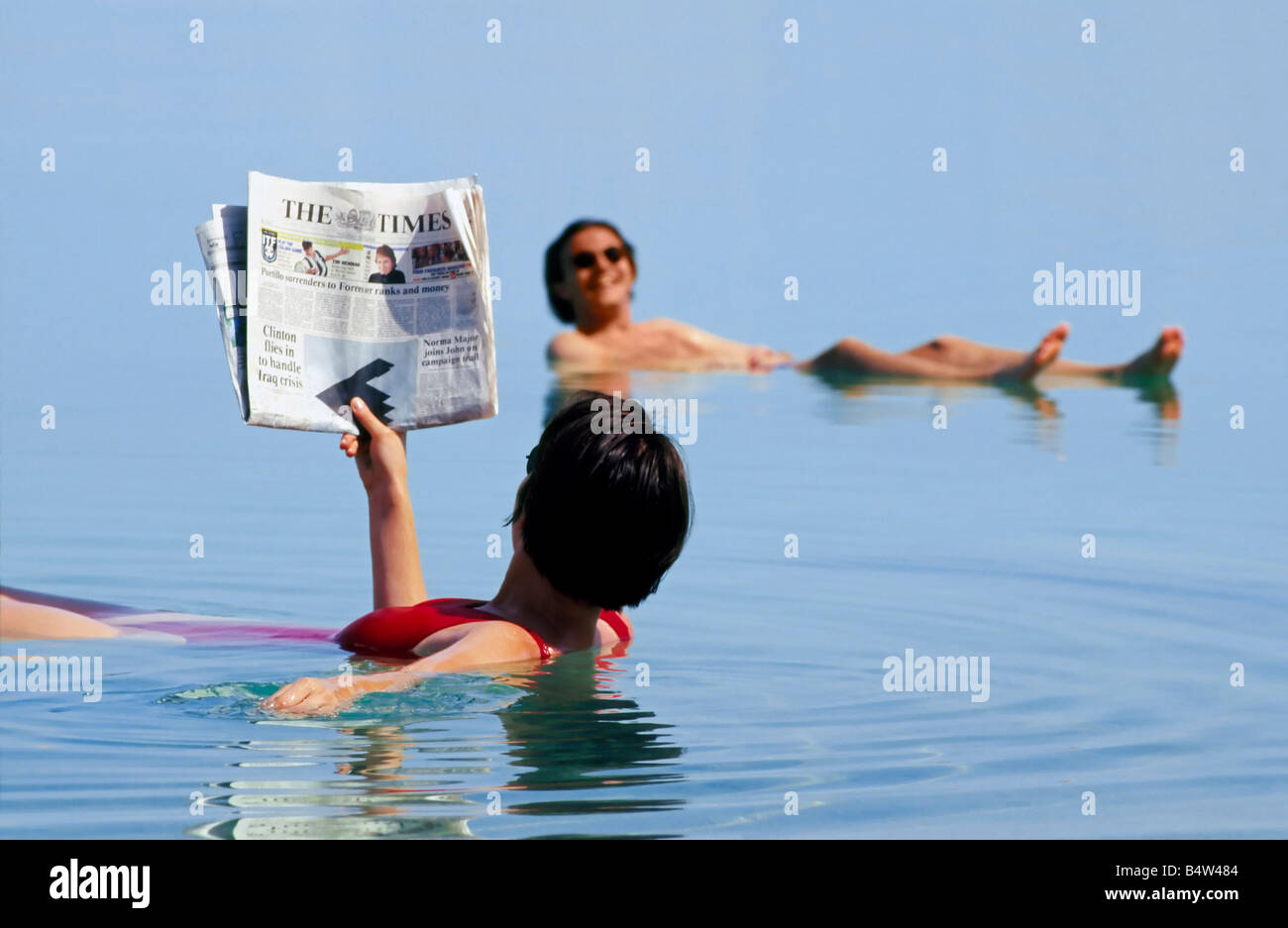 Two tourists 'floating' on the Dead Sea with one reading the Times newspaper. Stock Photo