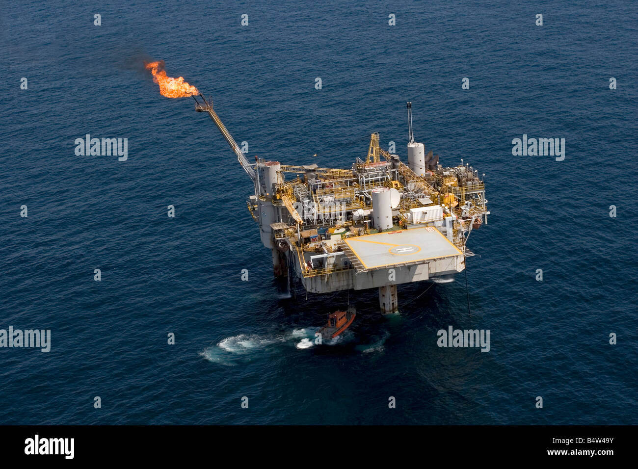 Aerial of offshore oil and gas production marine rig with safety boat as well as helicopter deck and safety flare, Gabon Stock Photo