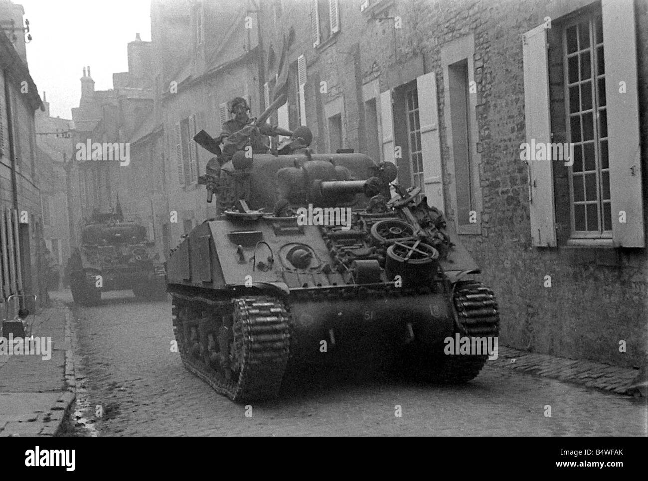 British troops in Sherman tanks roll throught the narrow cobbled streets of a Normandy town in Northern France shortly after the D Day landings begun the Allied invasion of the continent during World War Two July 1944 Stock Photo
