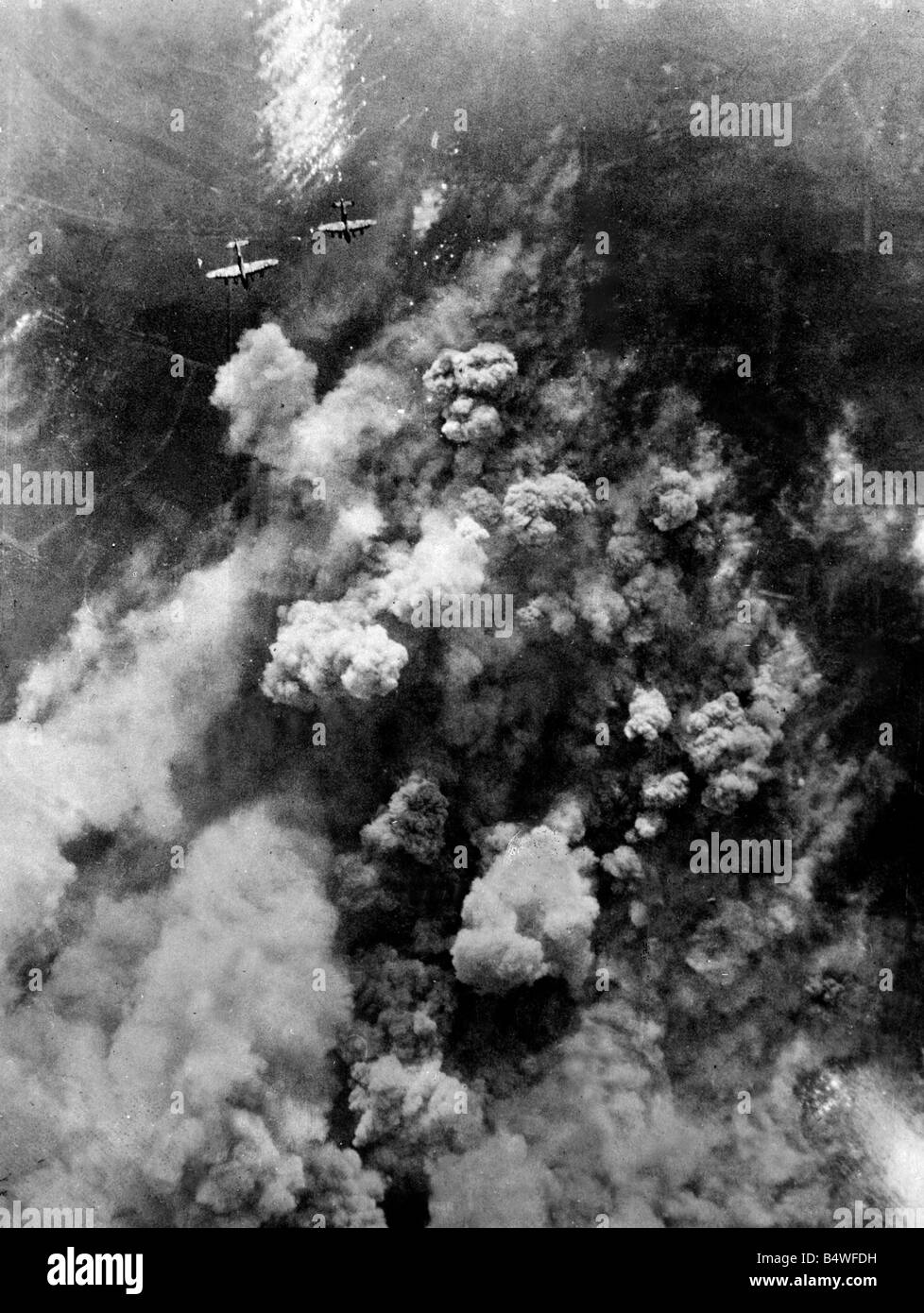 Dense smoke rising from the hail of bursting bombs as Avro Lancaster bombers of RAF Bombing command fly over the German town of Stock Photo