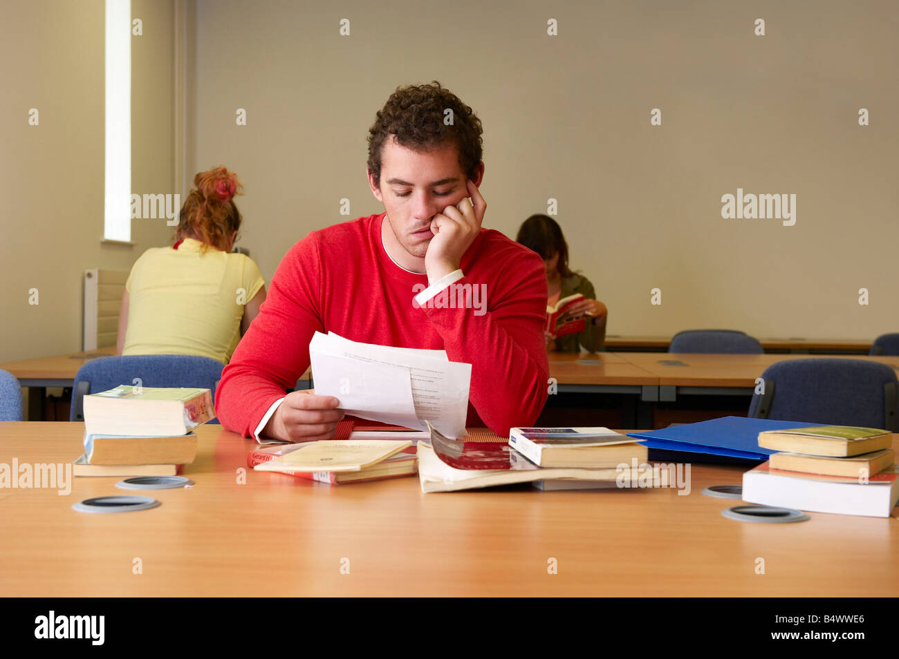 Bored young man seated at desk studying Stock Photo