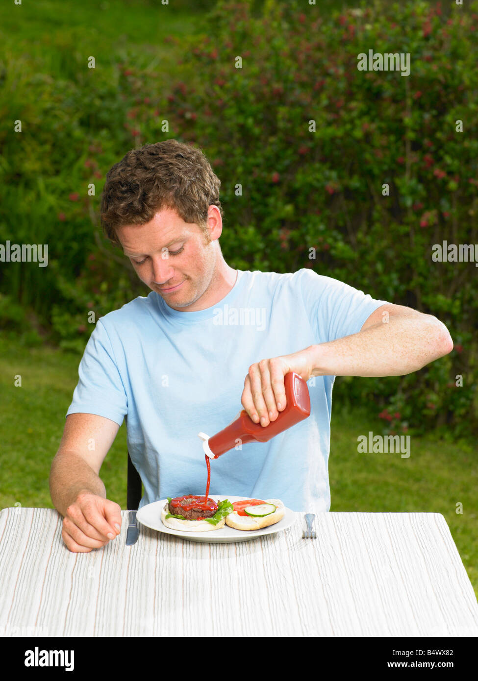 Young man pouring ketchup on burger Stock Photo Alamy