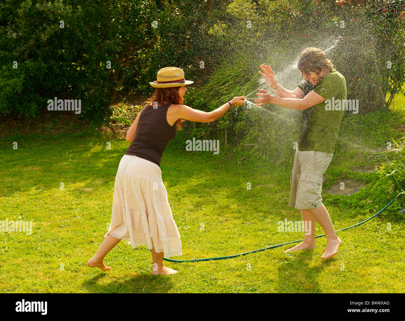Woman spraying man with garden hose Stock Photo