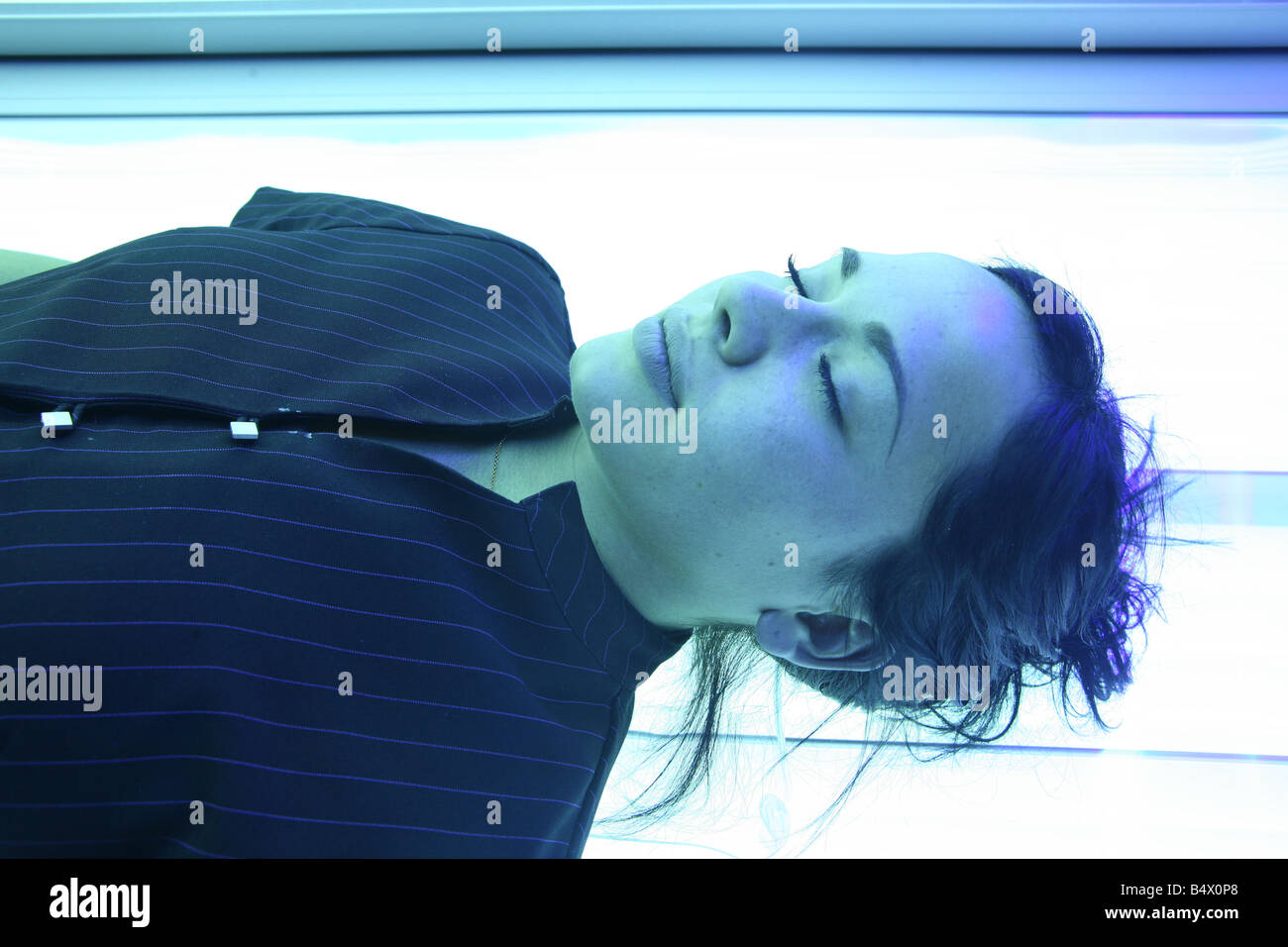 a portrait of a beautiful young woman laying on a sun bed in a tanning booth. The woman has brown hair Stock Photo