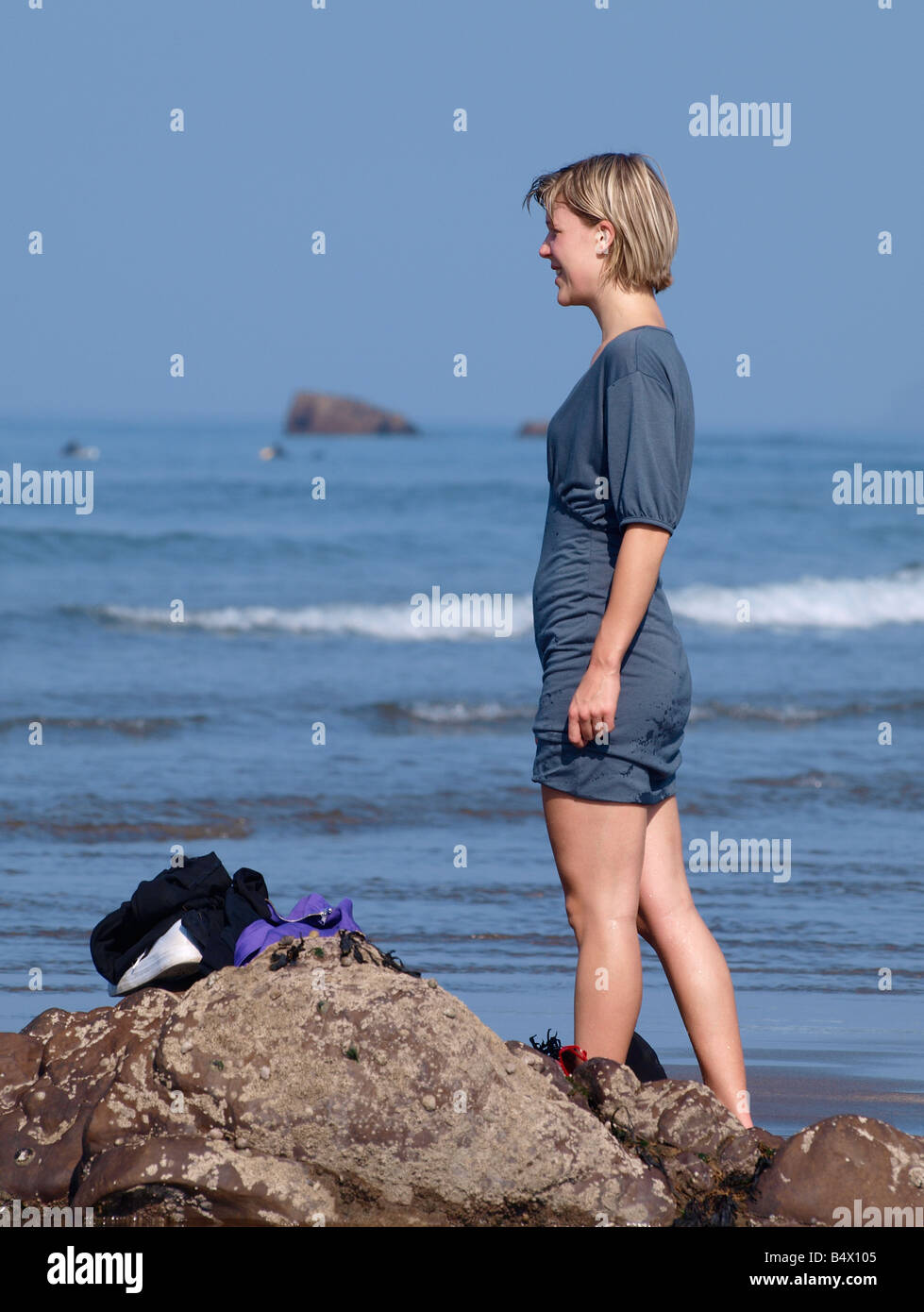 Young blonde woman standing on rocks looking out to sea Stock Photo