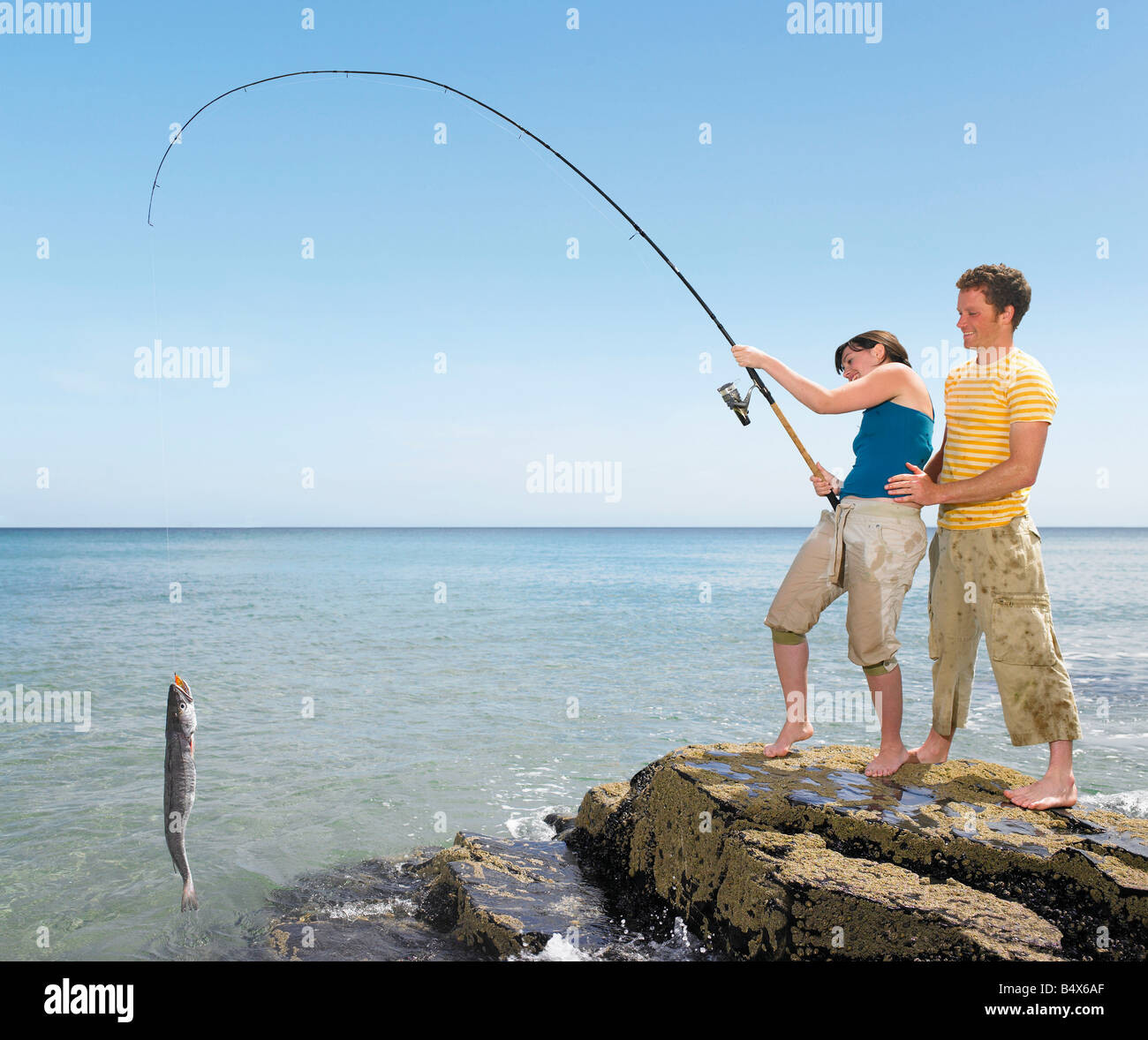 Couple landing a big fish off rocks Stock Photo