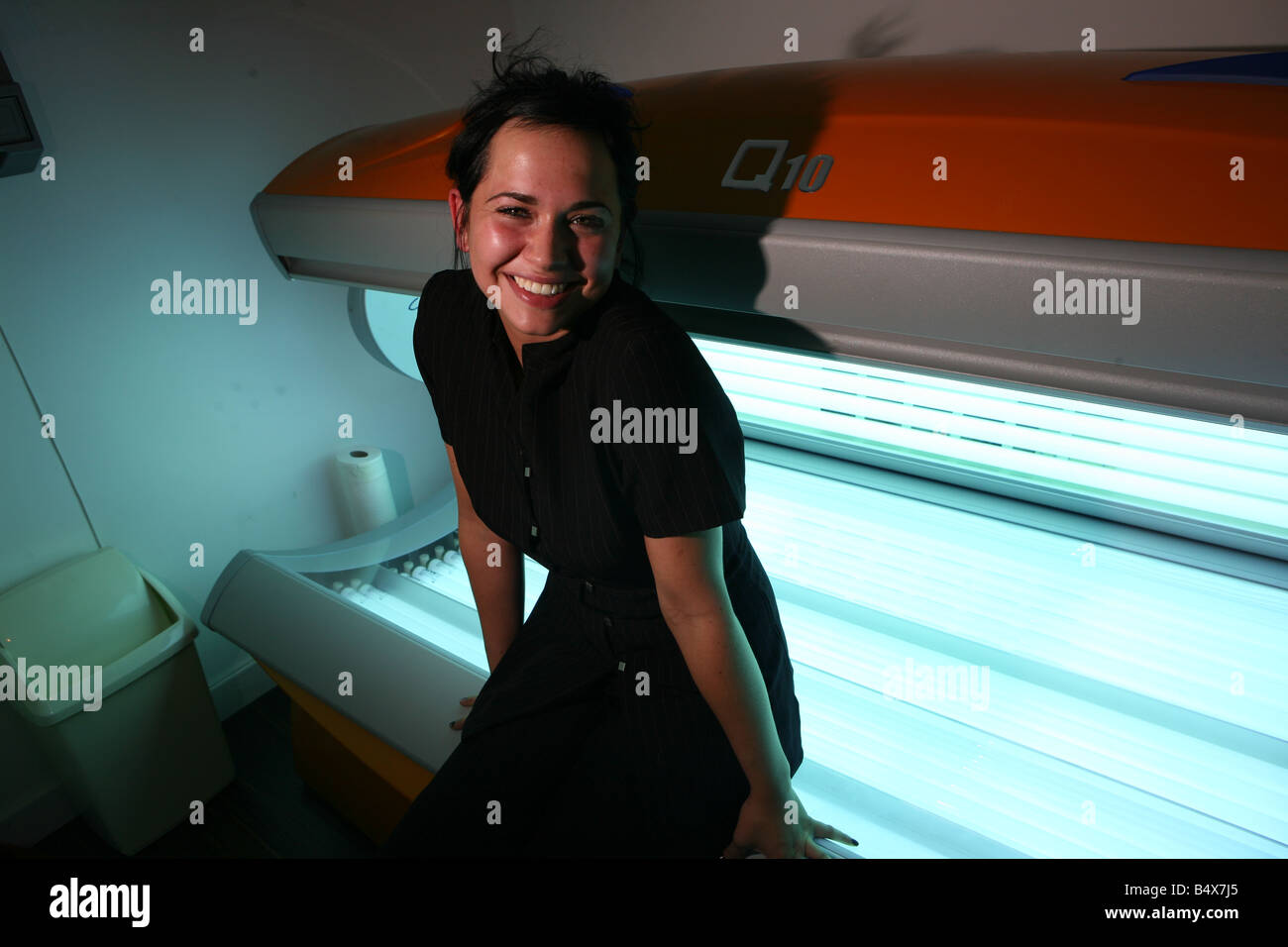 a portrait of a beautiful young woman laying on a sun bed in a tanning booth. The woman has brown hair Stock Photo