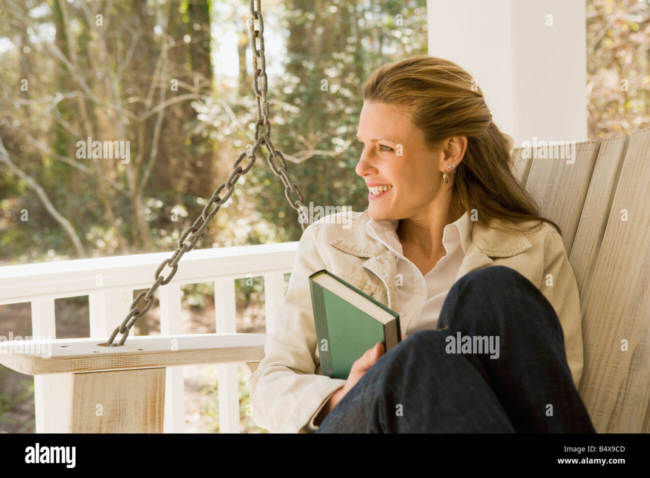 Woman relaxing with book on porch swing Stock Photo - Alamy