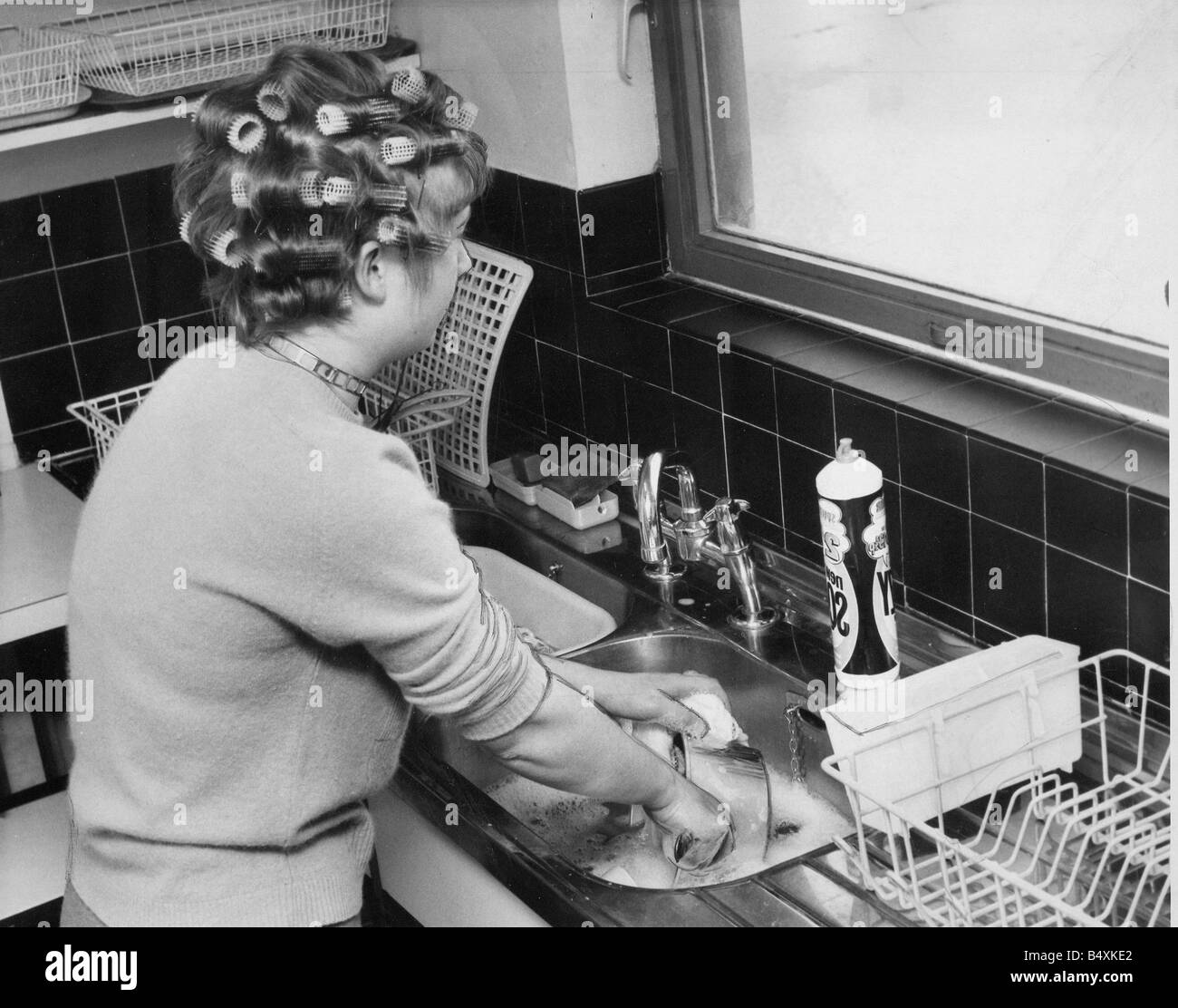 A woman is doing the washing up whislt waiting for her hair to curl before a night on the town Stock Photo