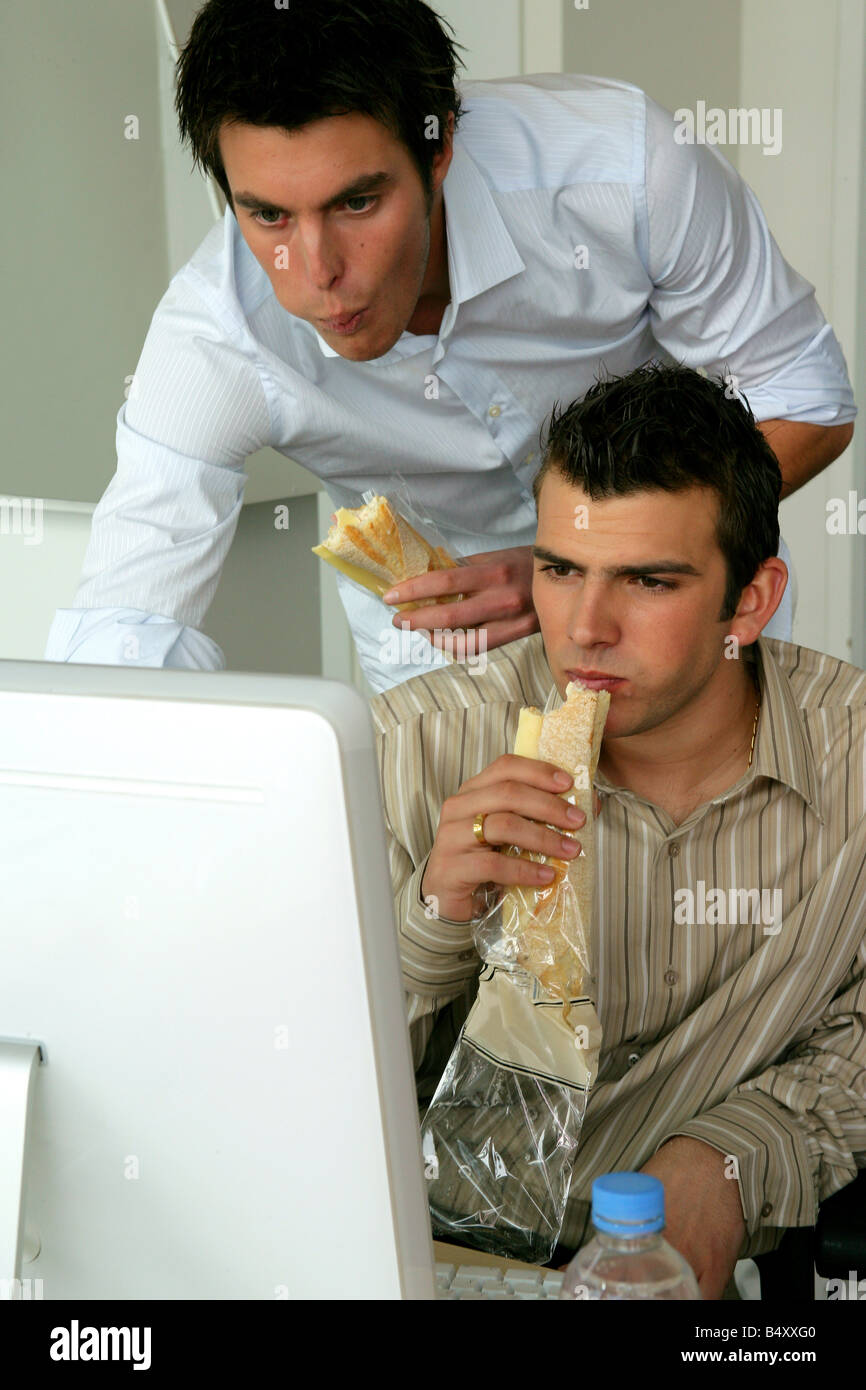 Two young men working on computer while eating sandwich Stock Photo - Alamy
