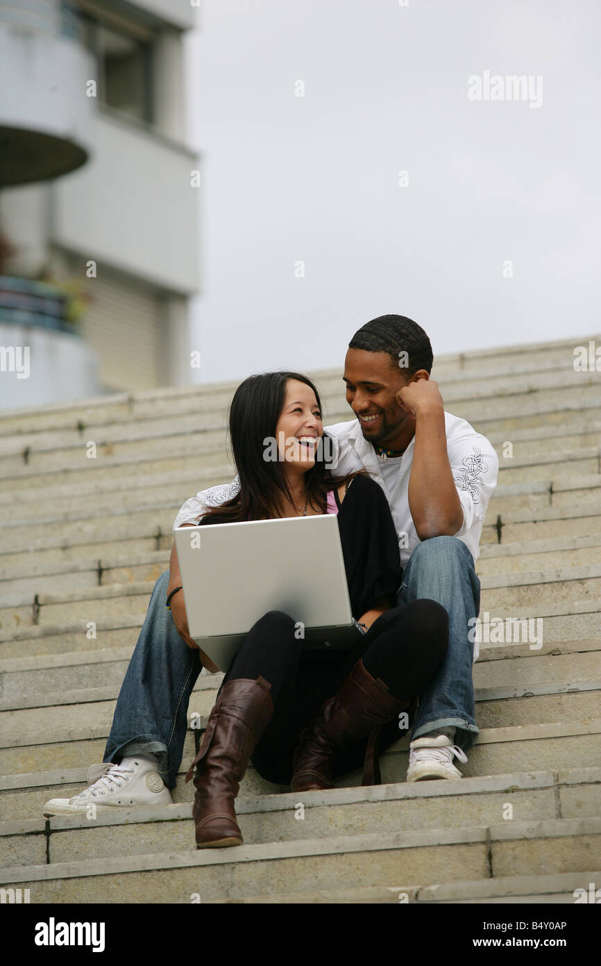 Young couple with laptop sitting on steps, smiling Stock Photo - Alamy
