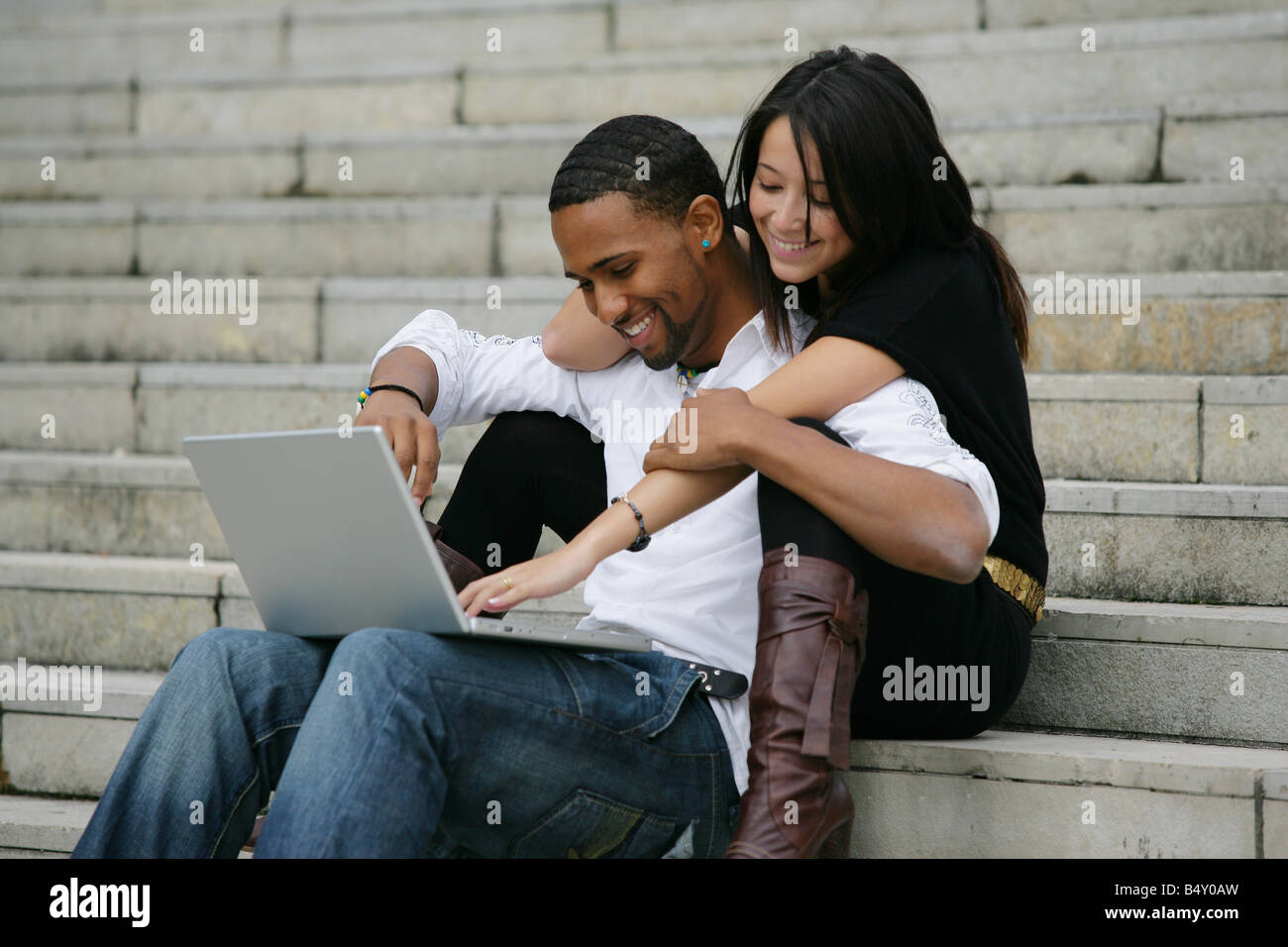 Young couple with laptop sitting on steps, smiling Stock Photo - Alamy