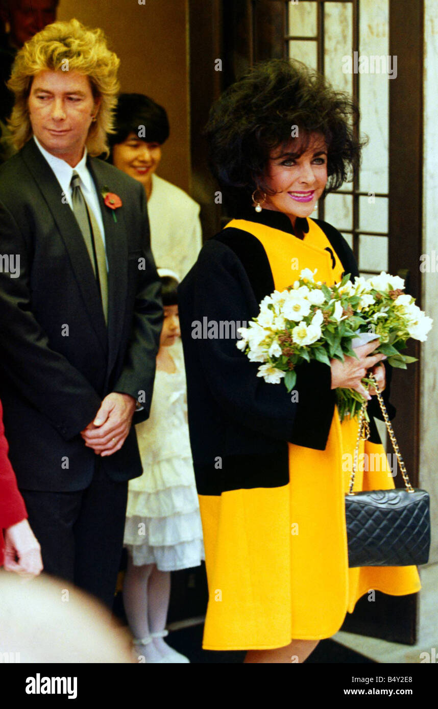 Elizabeth Taylor and her 8th husband construction worker Larry Fortensky arrive back at the airport from their honeymoon Holding bouquet of flowers wearing bright yellow outfit and purple lipstick Her partner is wearing a suit with a remembrance day poppy in the lapel Little girl in the background dressed in white 1990s Marriage honey moon Liz Taylor Stock Photo