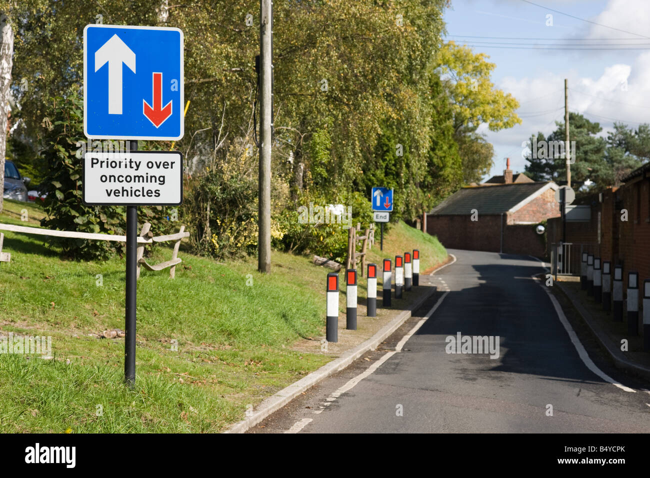 Single carriageway narrow road with sign that says priority over oncoming vehicles Stock Photo