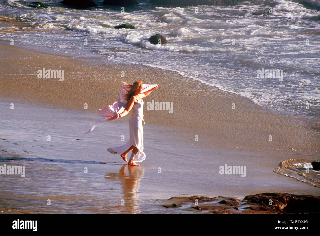 Woman in white dress and shawl feeling free and happy under sunny skies on sandy California shore Stock Photo