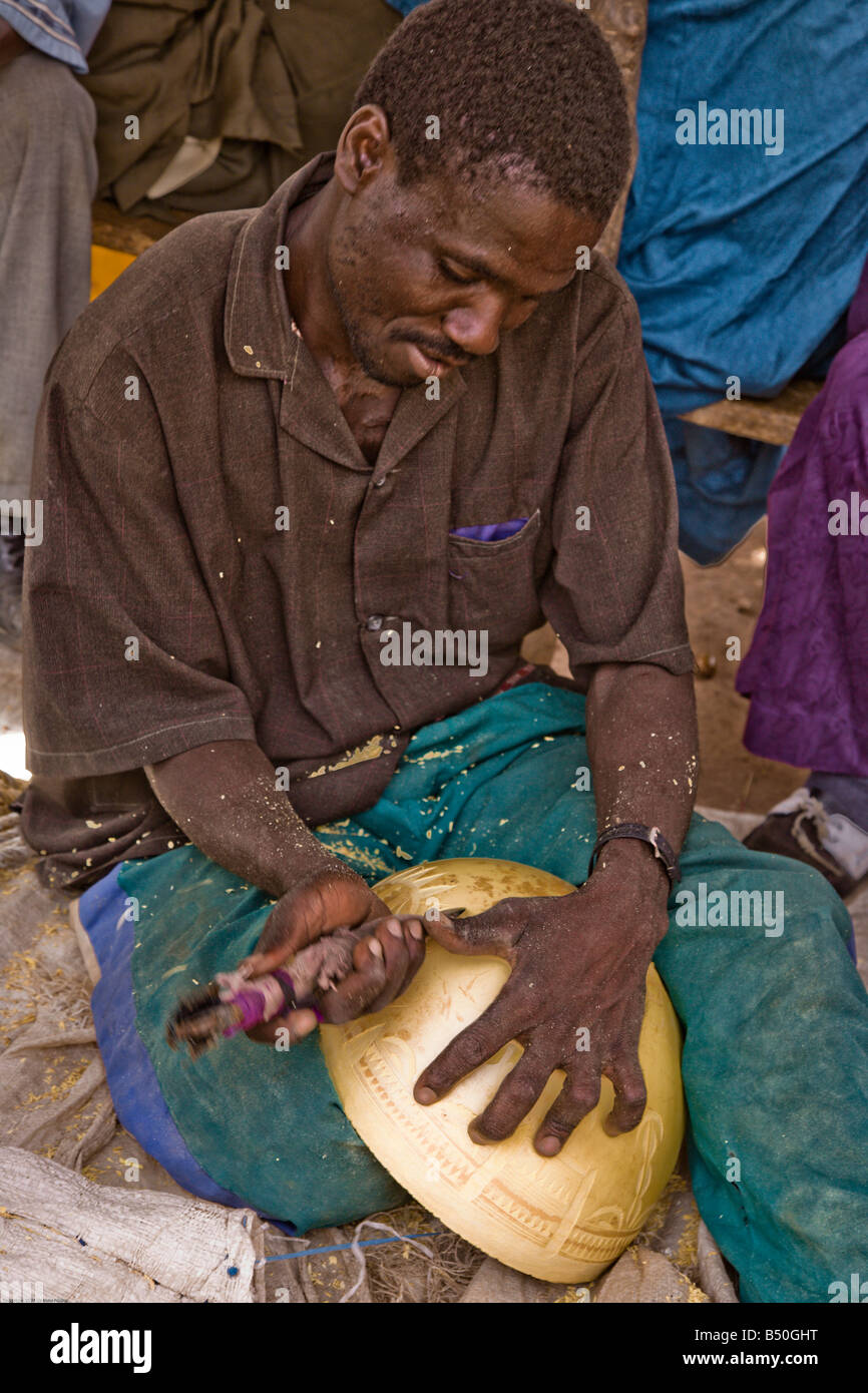A man sits in his stall at the weekly market in Torodi, Niger carving a calabash to sell. Stock Photo