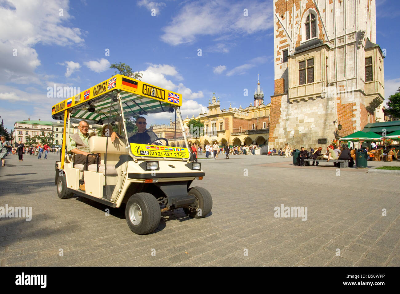 An electric tourist car city tour in the Main Market Square of Krakow in Poland with the base of the Town Hall Tower right. Stock Photo