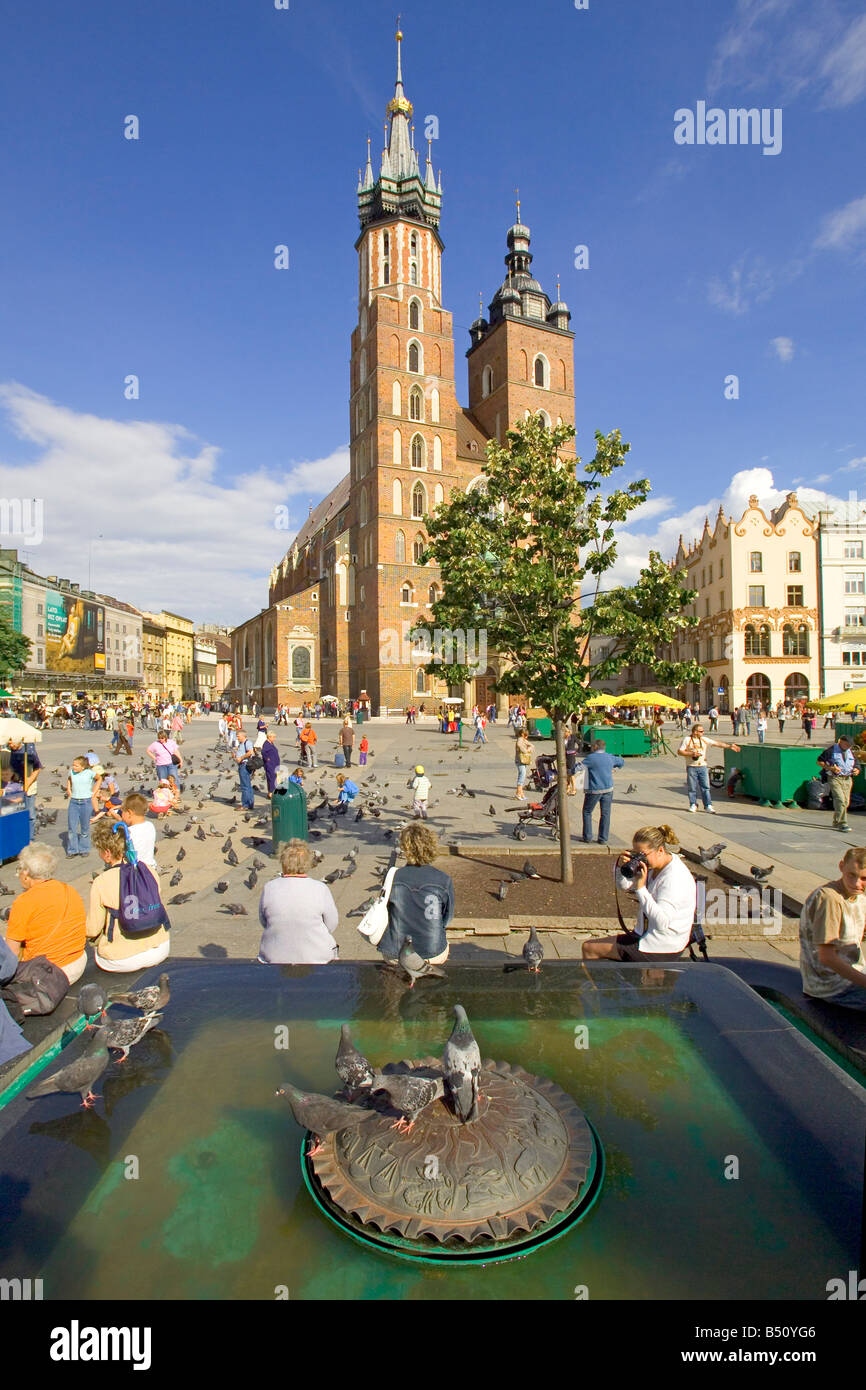 Ornamental water feature and tourists in the Main Market Square of Krakow with St. Mary's Basilica Gothic church behind. Stock Photo