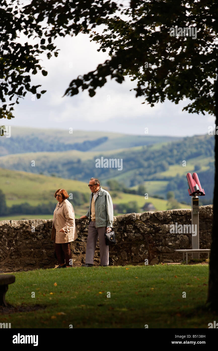 An elderly couple walk in the countryside next to a stone wall and valley in the background Stock Photo