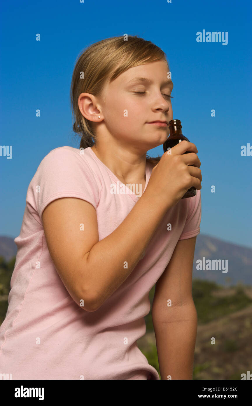 Young girl smelling a small bottle with blue sky background Stock Photo