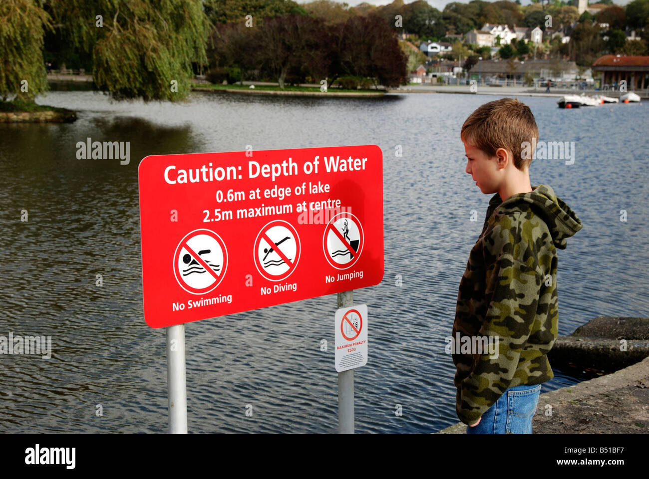 a young boy reading a safety warning sign by a lake in helston,cornwall,uk Stock Photo