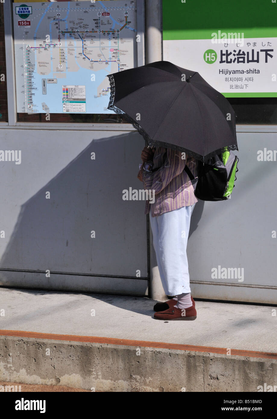 Japanese tram or streetcar stop at Hijiyama-bashi, Hiroshima, Japan, showing lady waiting for tram with umbrella sunshade Stock Photo