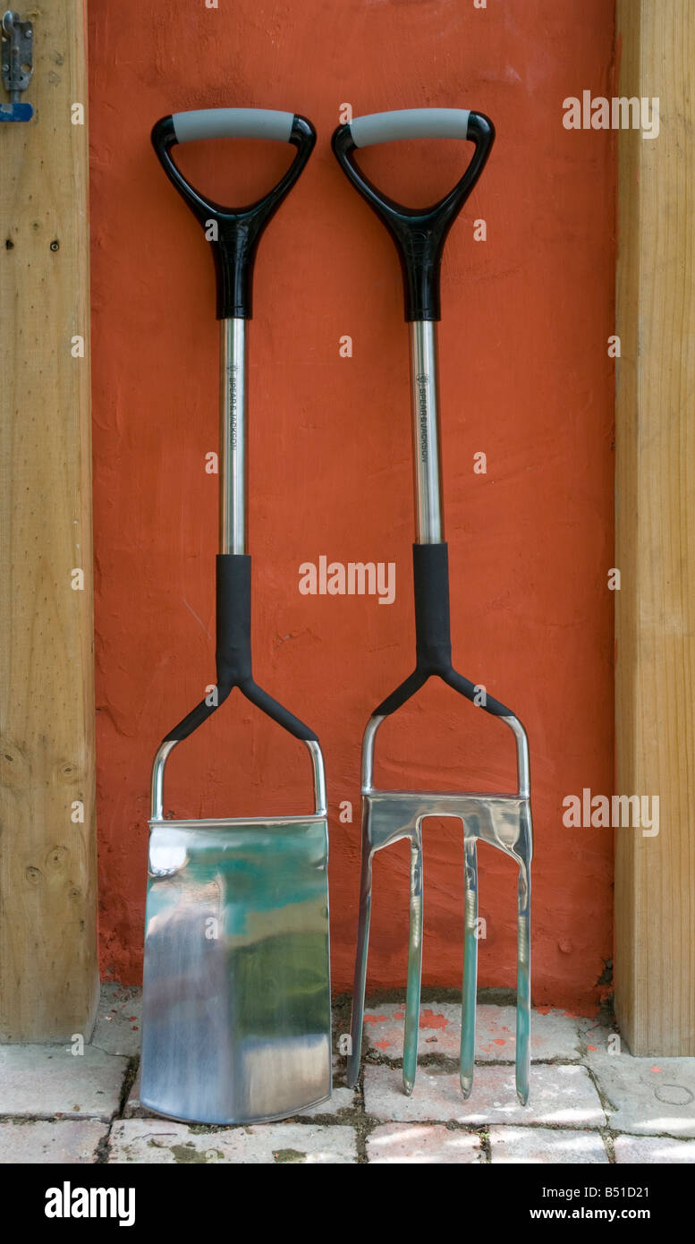 Well designed, high quality stainless steel garden fork and spade leaning against a colourful lime washed stucco wall Stock Photo