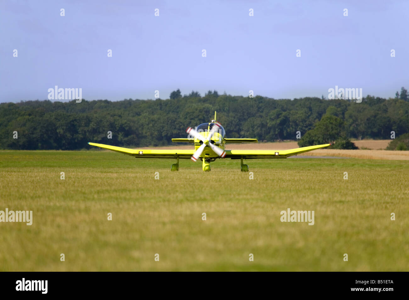 A yellow single propeller light aircraft taxiing on grass Stock Photo