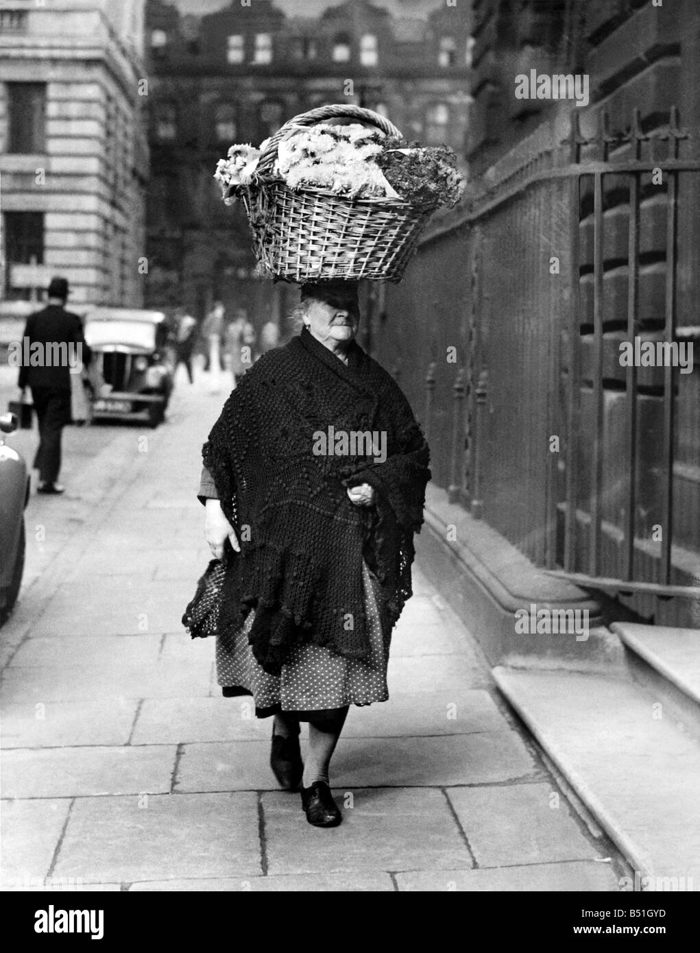 This 68 year-old flower seller of Liverpool presents an unusual picture as she carries her flowers on her head from the market to her stall. Although she has been carrying them in this fashion for 52 years she says that she never suffers from head-aches or stiff neck. This Lancashire Carmen Miranda prefers to remain anonymous. November 1945 P000080; Stock Photo