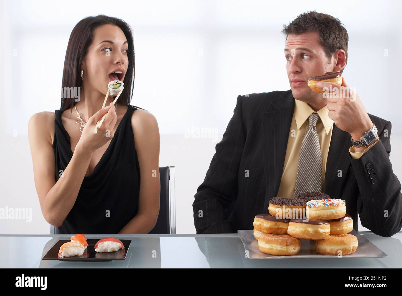 Woman Eating Sushi and Man Eating Doughnuts Stock Photo