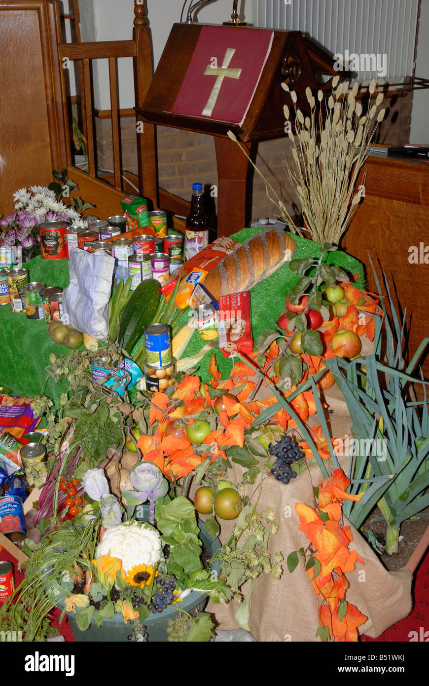 Harvest festival display of fruit, vegetables and tinned and bottled goods in Church of England church with lectern and cross Stock Photo