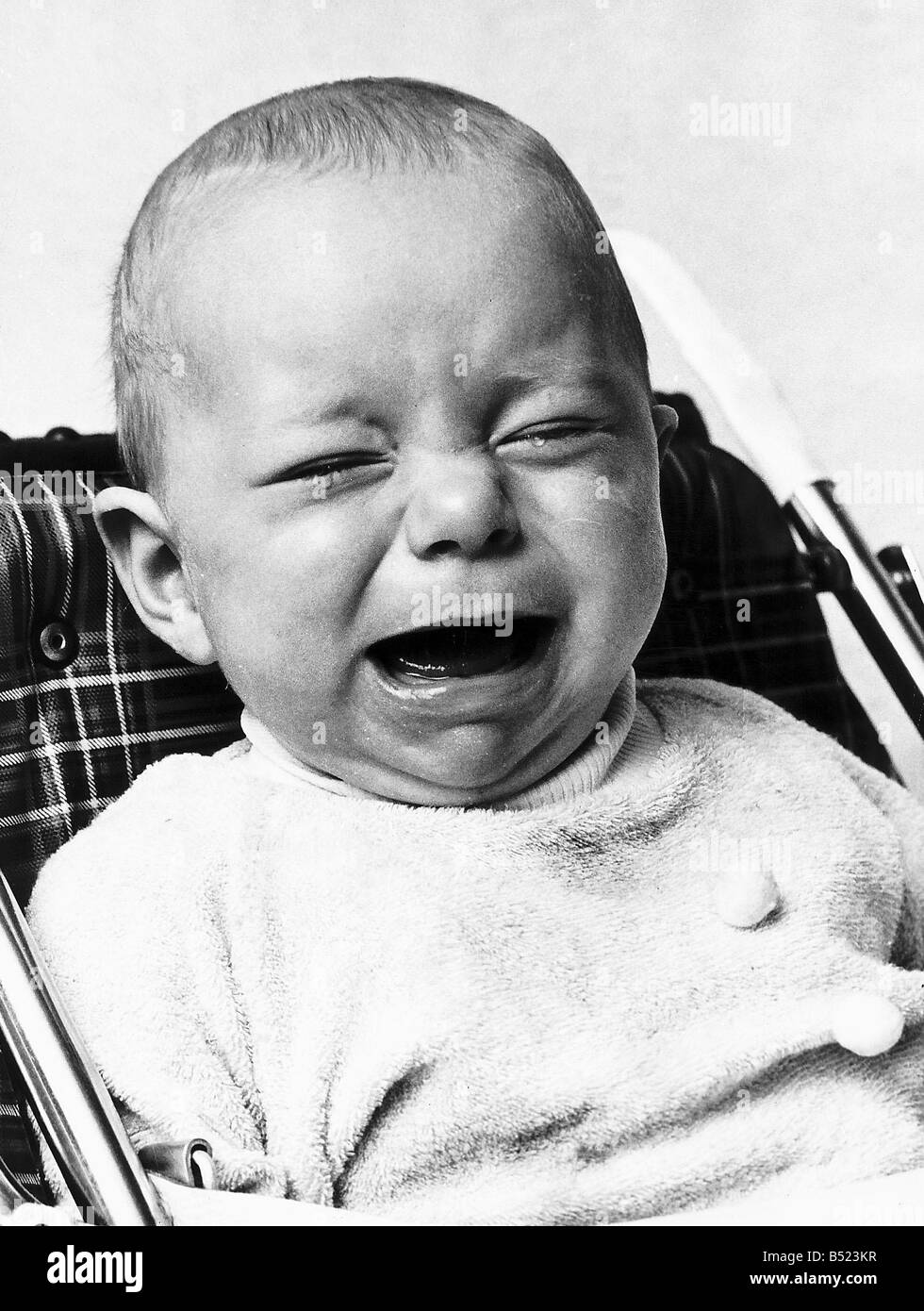 A baby crying as he sits in his high chair January 1973 Stock Photo