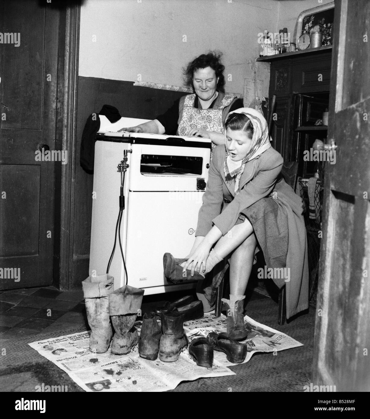 Housewife Mrs. Gladys Coates changes into better footwear after leaving the the mud covered ones in front of the fire at the home of Mrs. Minnie Bagnall. ;January 1953 ;D531 Stock Photo