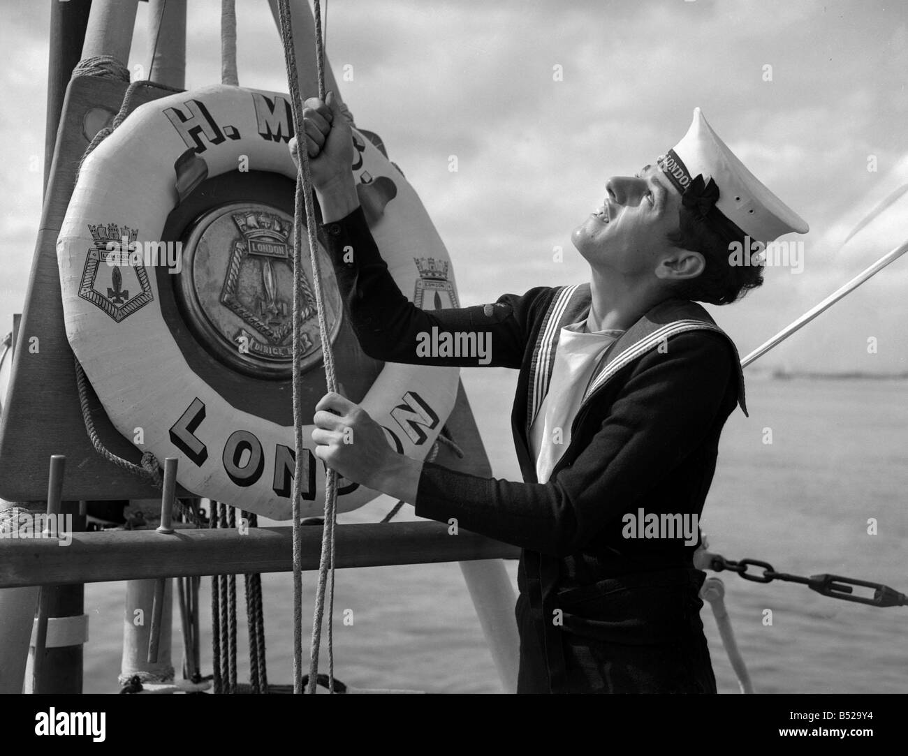 A naval rating raising the white ensign aboard the County Class cruiser HMS London which was damaged in the rescue attempt of HMS Amethyst in the Yangtze river Royal Navy pulling on rope lift belt ships crest sailor 1940s Stock Photo