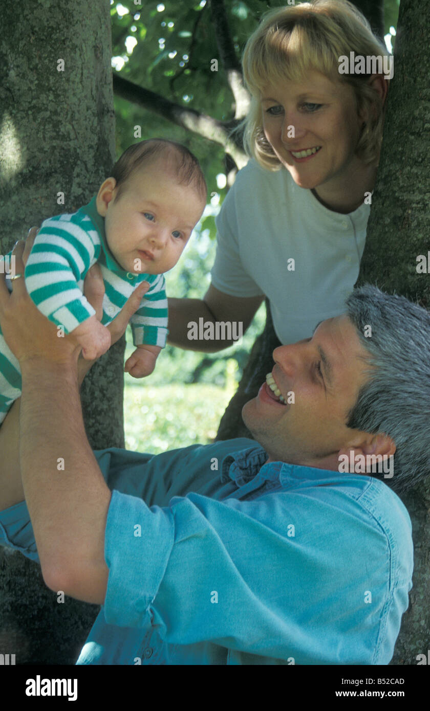 parents sitting under tree and playing with their little baby Stock Photo