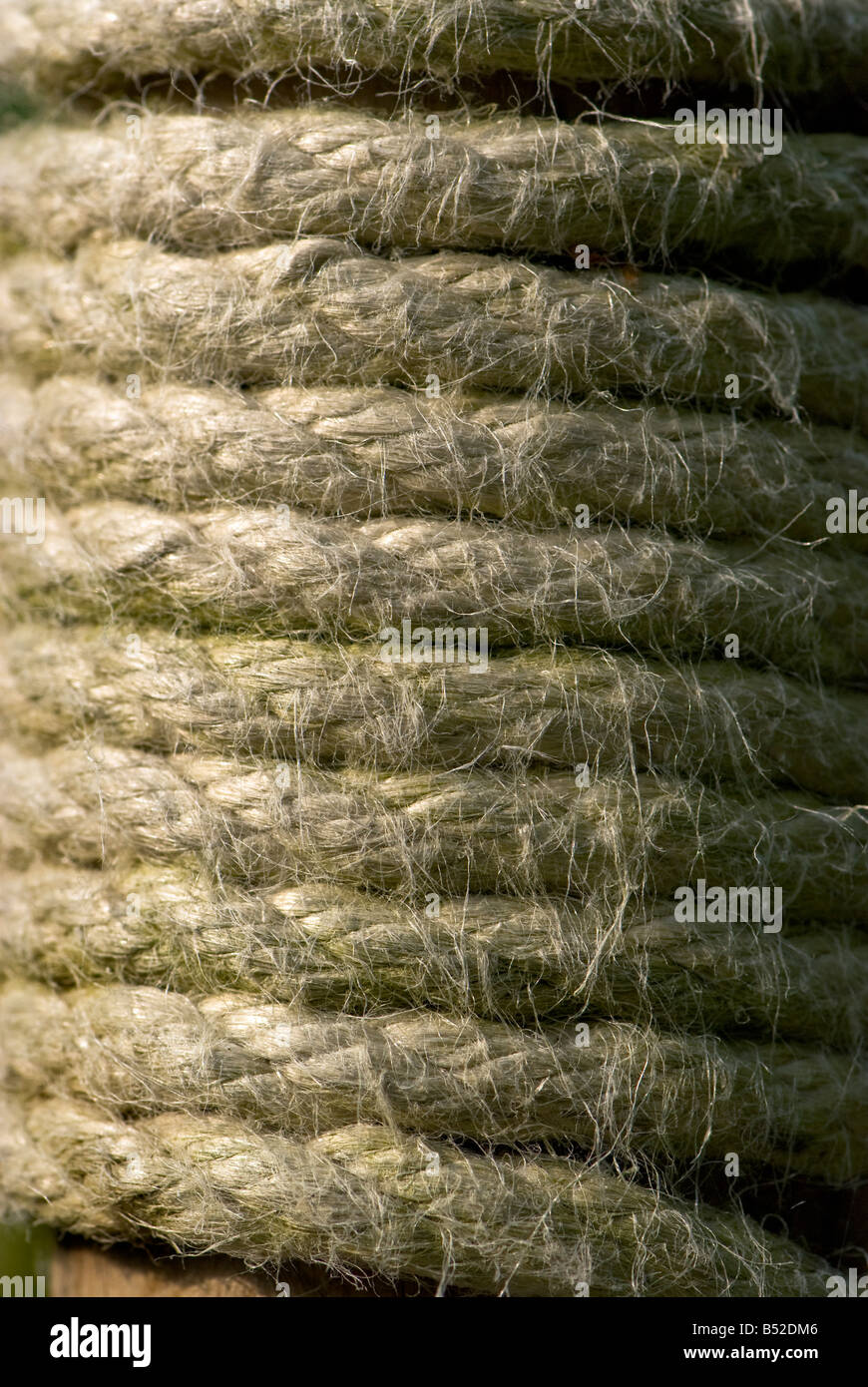 Close-up of thick rope wound tightly around a wooden post, showing its coarse fibres. Stock Photo