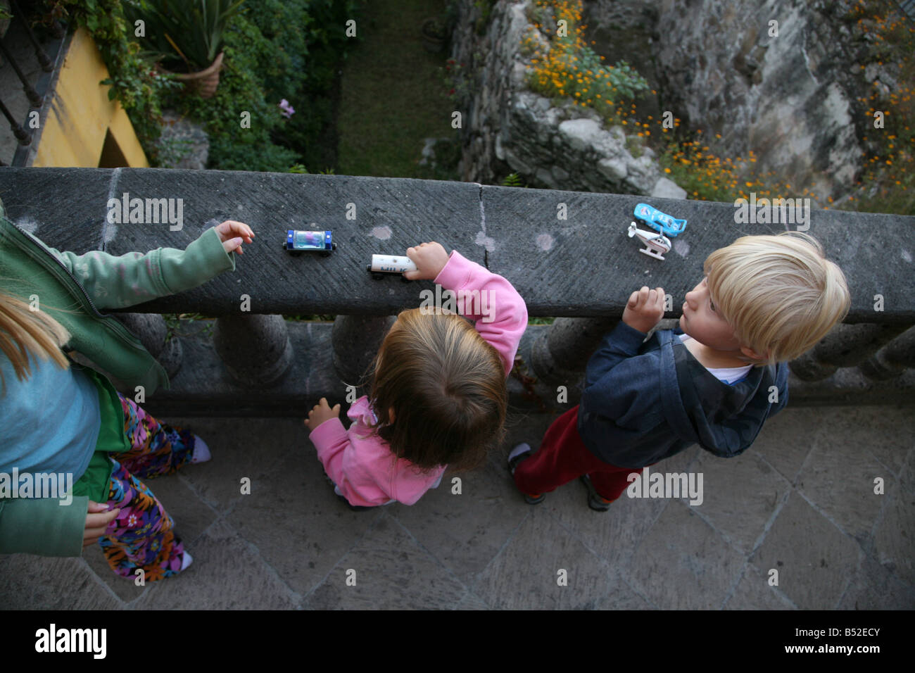 Children playing outside with toy cars on an old stone balcony. Little boy listens attentively to older girl explain the rules Stock Photo