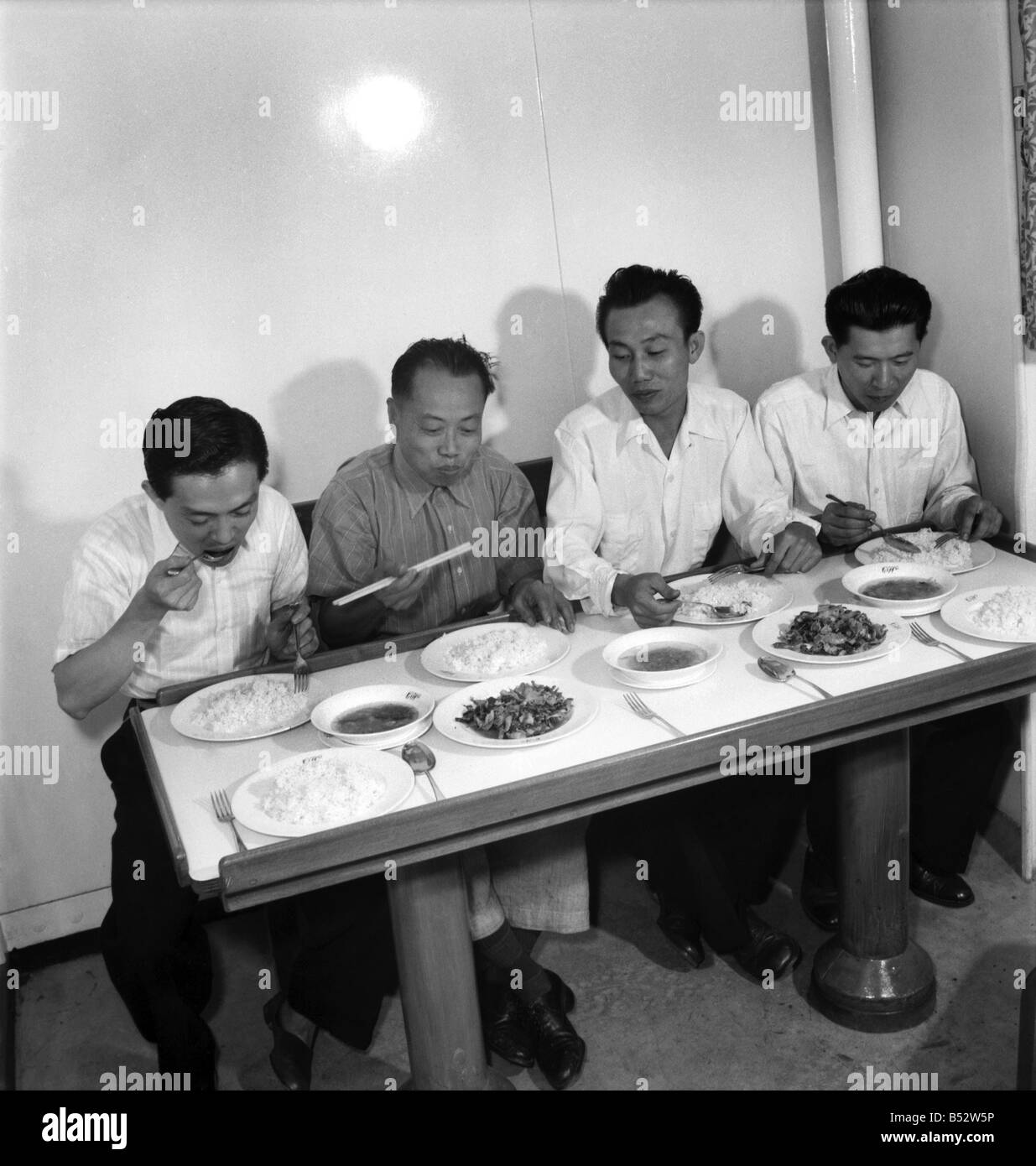 A Chinese member of the crew of the cargo vessel Stanley Angwin demonstrate to his shipmates the correct way to eat using chop s Stock Photo