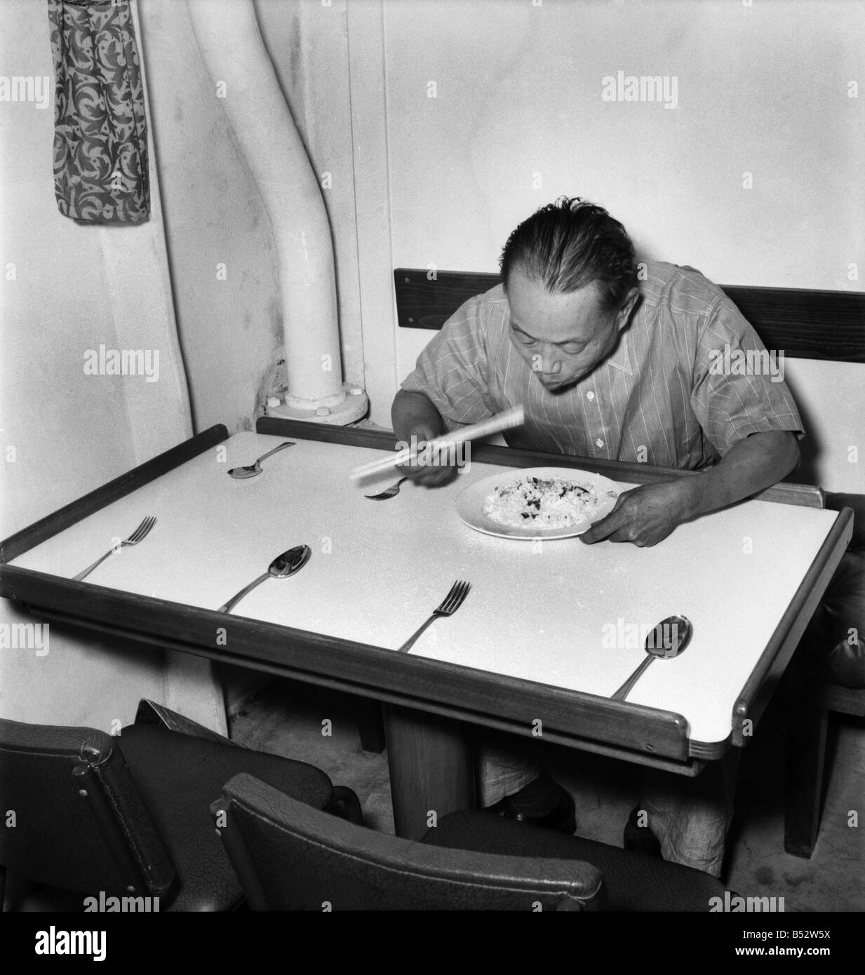 A Chinese member of the crew of the cargo vessel Stanley Angwin demonstrate the correct way to eat using chop sticks. Aboard. Ju Stock Photo