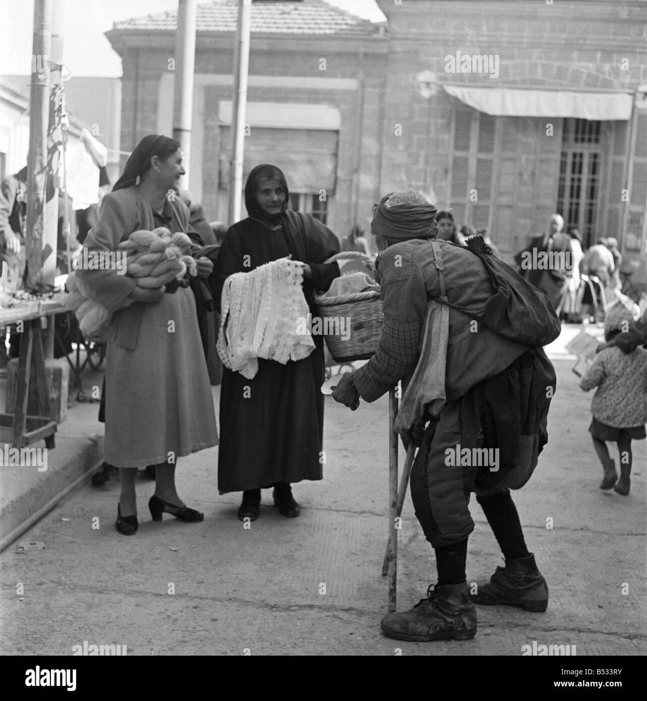 Traders at the Ladies Bazaar which opens every Friday in Nicosia, Cyprus,. The market sells items as diverse as lace, silk, embroideries, fruit and food. Our picture shows: A beggar approaching two women out shopping. November 1952 C1105-005 Stock Photo