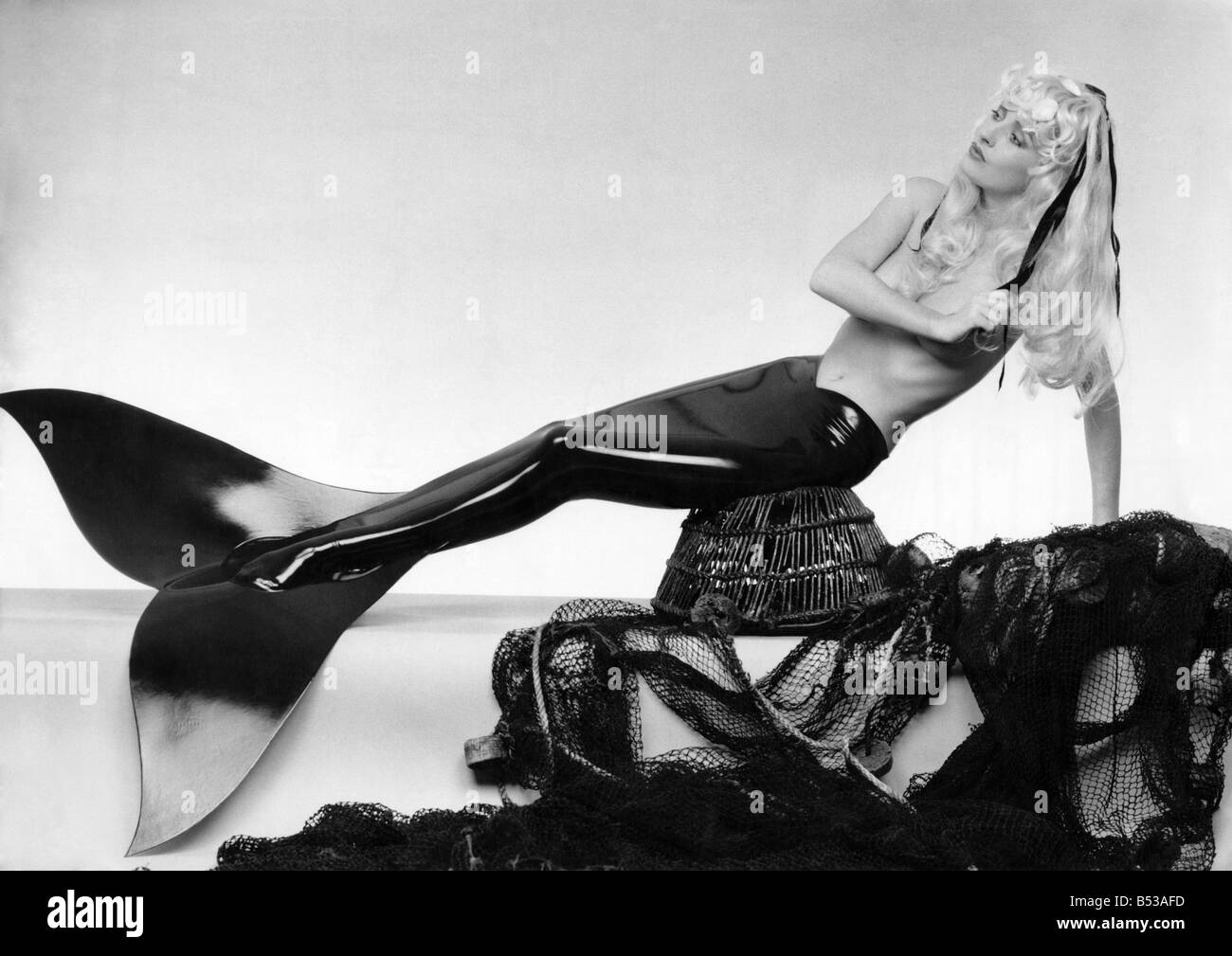Model wears a mermaid costume, sitting on a fishing basket reclining on fishing nets. She wears a tail and nothing else. Feb. 19 Stock Photo